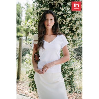 Woman in white outfit stands by flowering bush