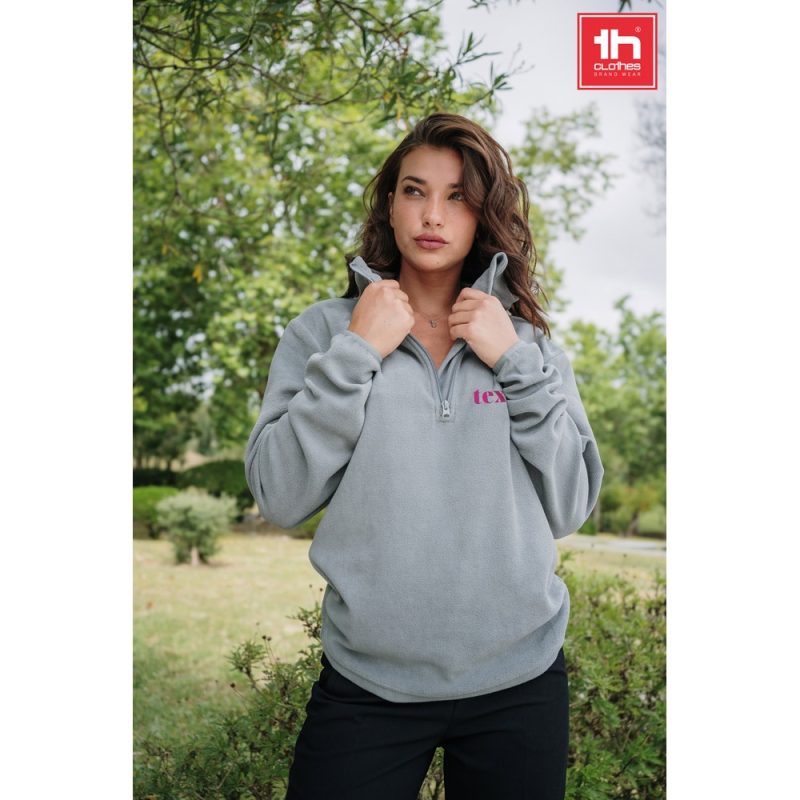 Woman wearing grey fleece outdoors with foliage background.