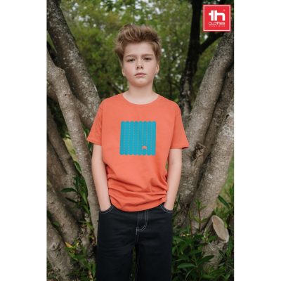 Boy wearing orange T-shirt standing by tree.