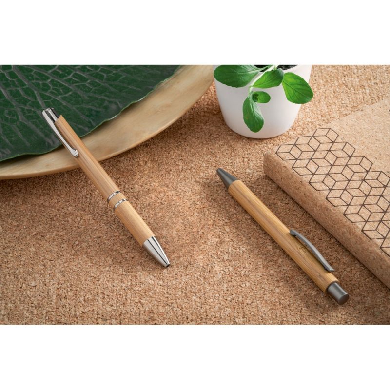 Two bamboo pens on cork desk with notebook.