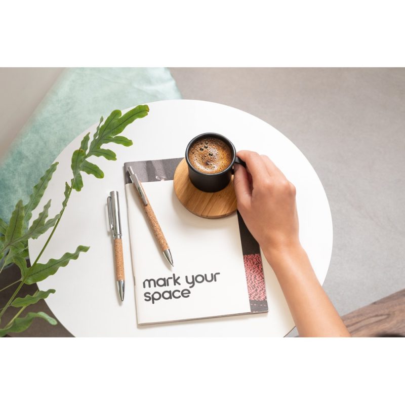 Person holding coffee cup with journal and pens.