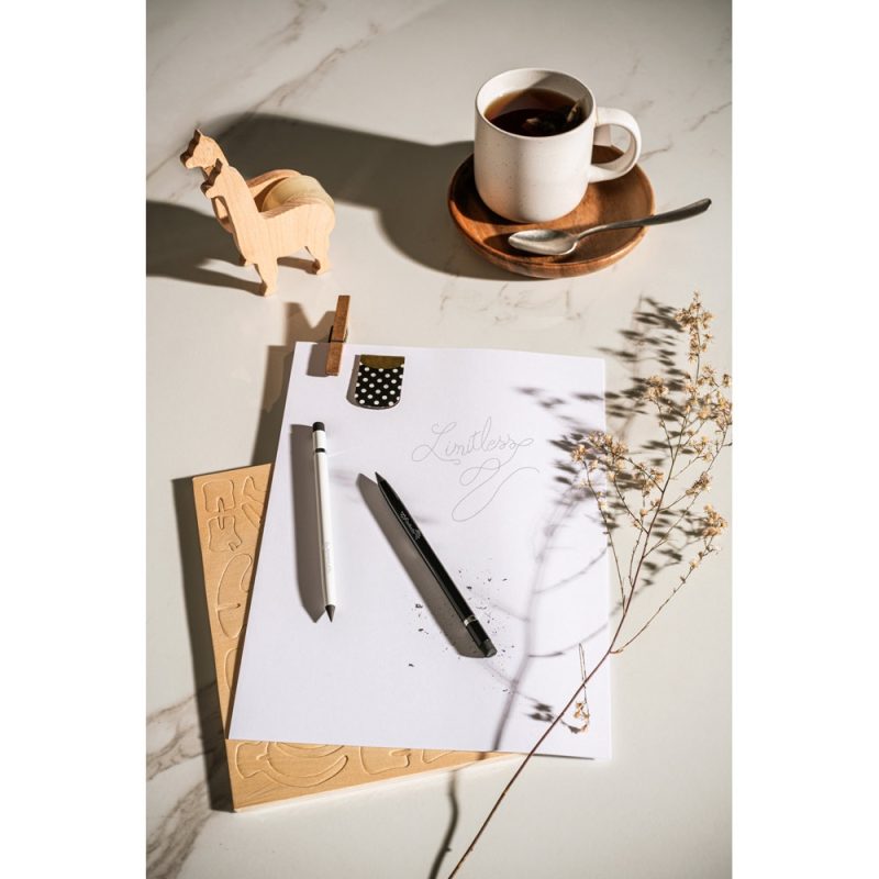 Notebook with pens, coffee, and wooden horse on desk.