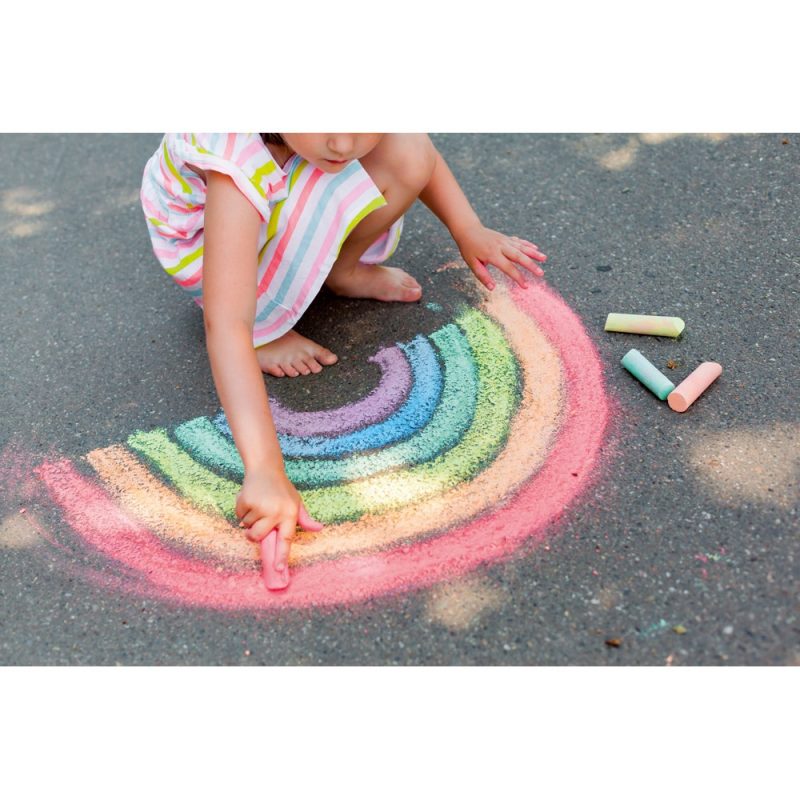 Child drawing rainbow with colourful chalks on pavement.