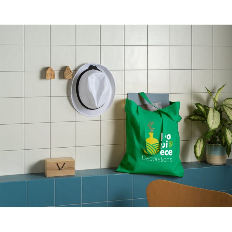 White hat, green tote bag, near plant on tiles.