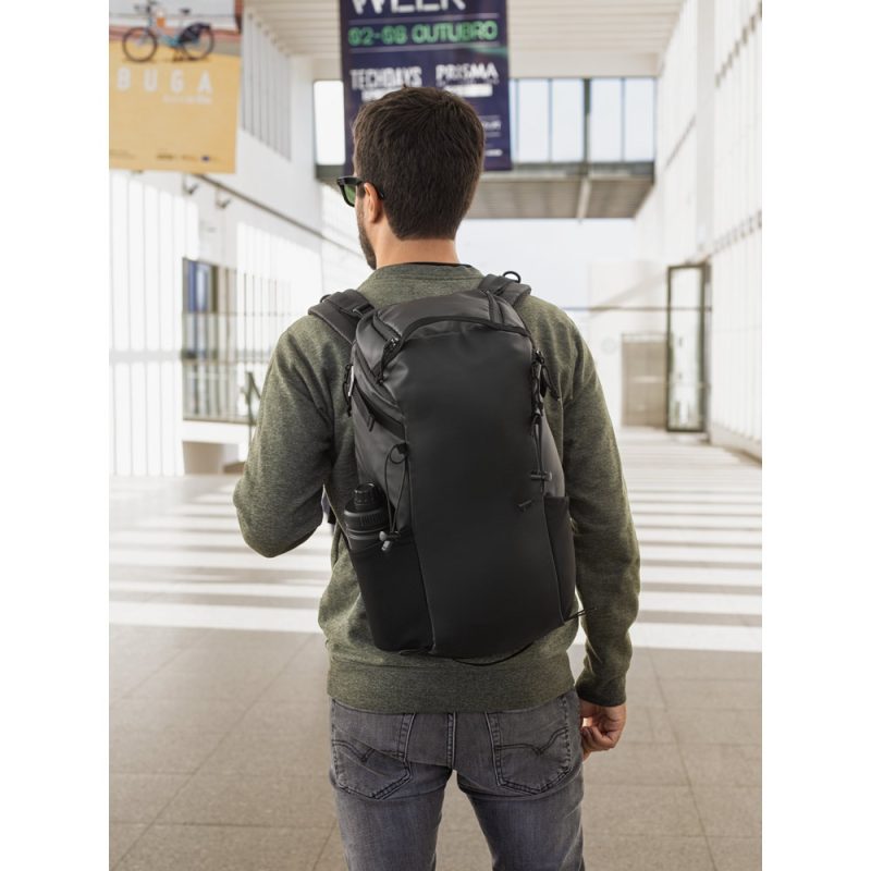 Person wearing black backpack in a modern hallway.