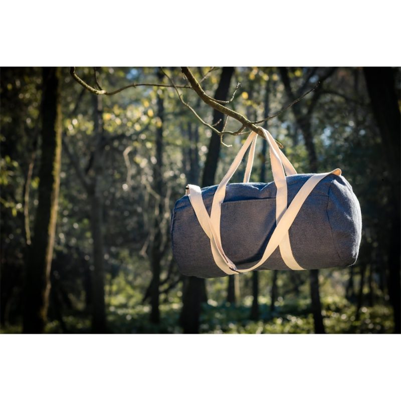 Blue duffel bag hanging from tree in forest.