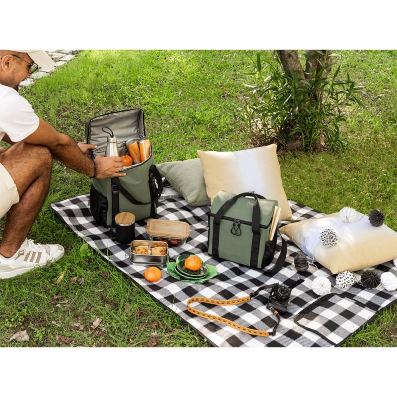 Man setting up picnic on checked blanket in park.