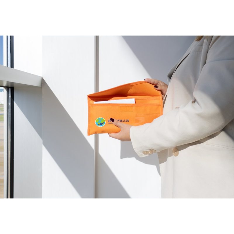 Person holding orange travel wallet by window.