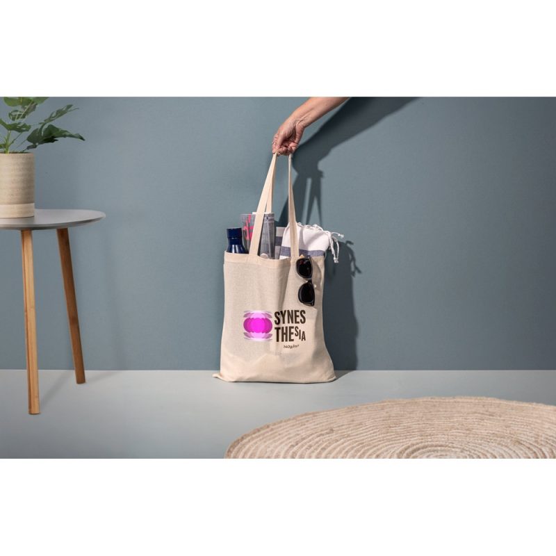 Hand holding tote bag with items on table.