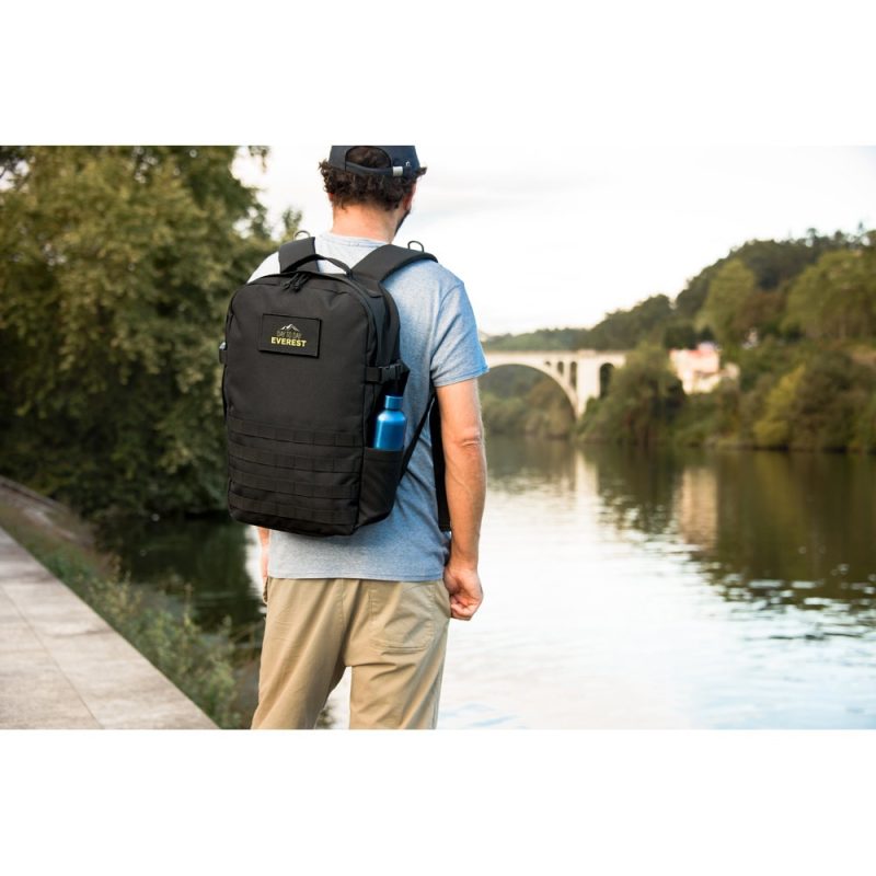 Person with backpack walking by river with bridge.