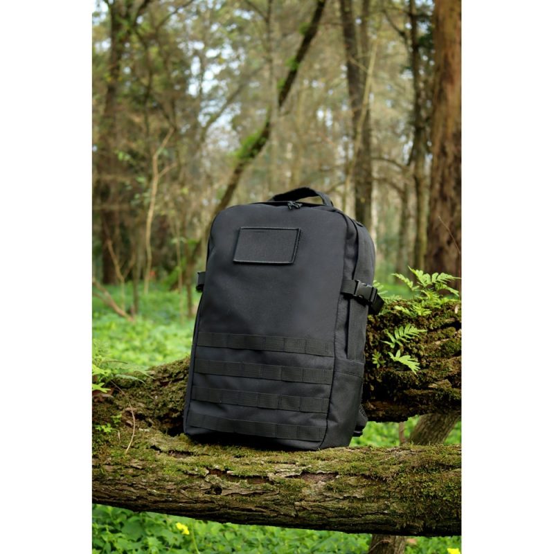 Black backpack on a mossy log in forest.