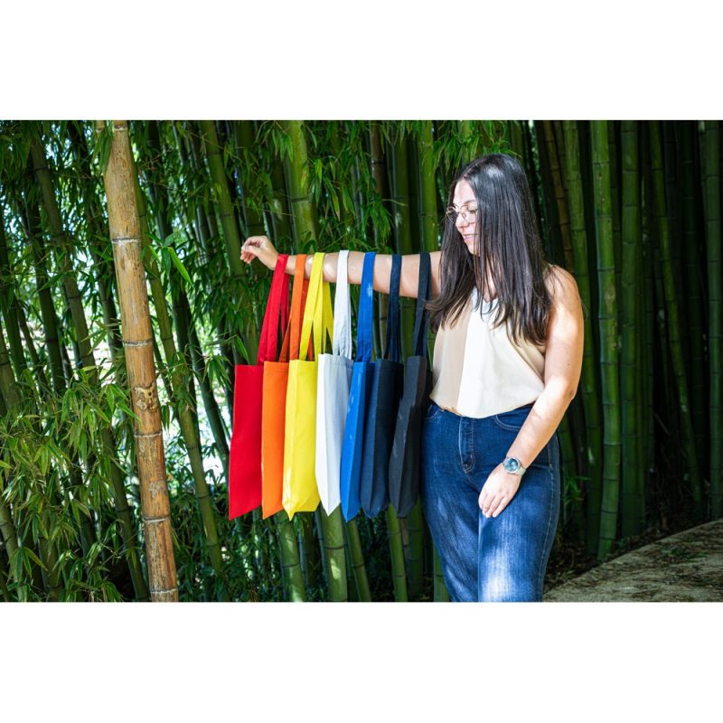 Woman holding colourful tote bags in bamboo forest.
