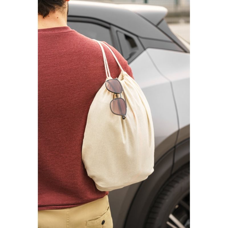 Person with beige bag and sunglasses near car.