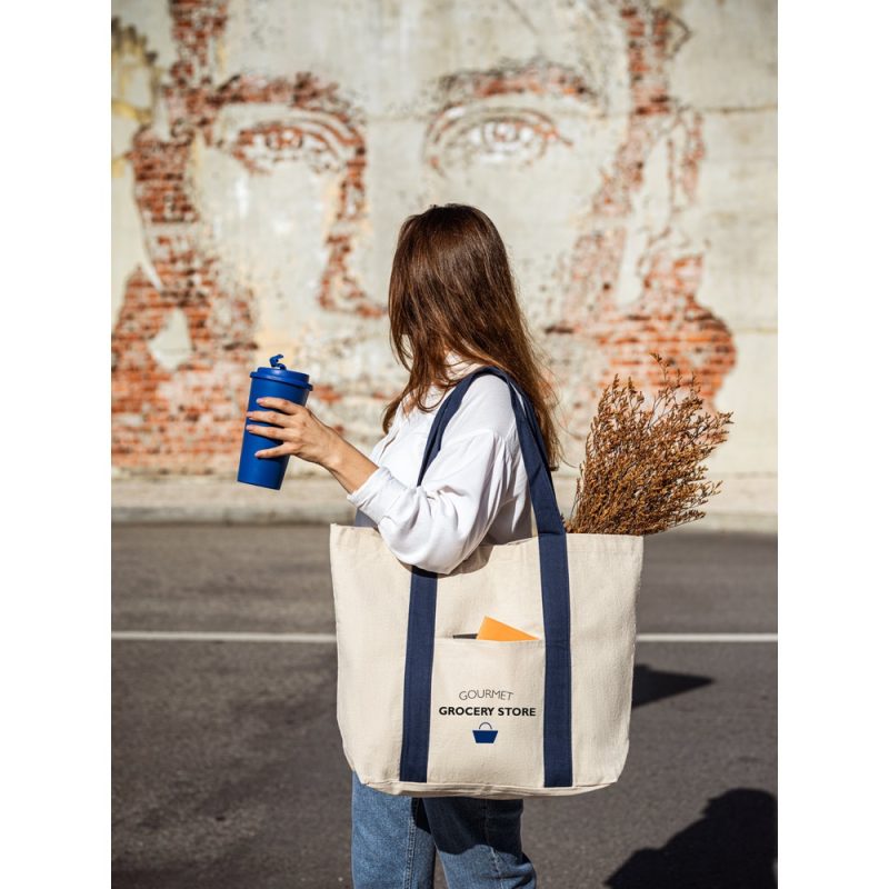 Person with reusable bag and cup near mural.