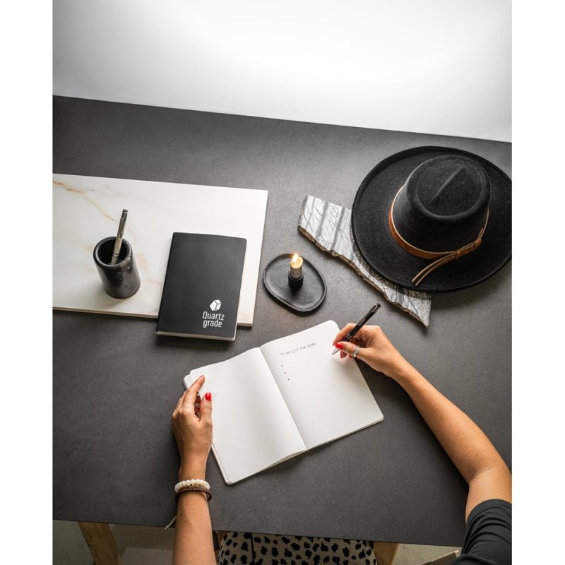 Person writing in notebook on desk with hat.