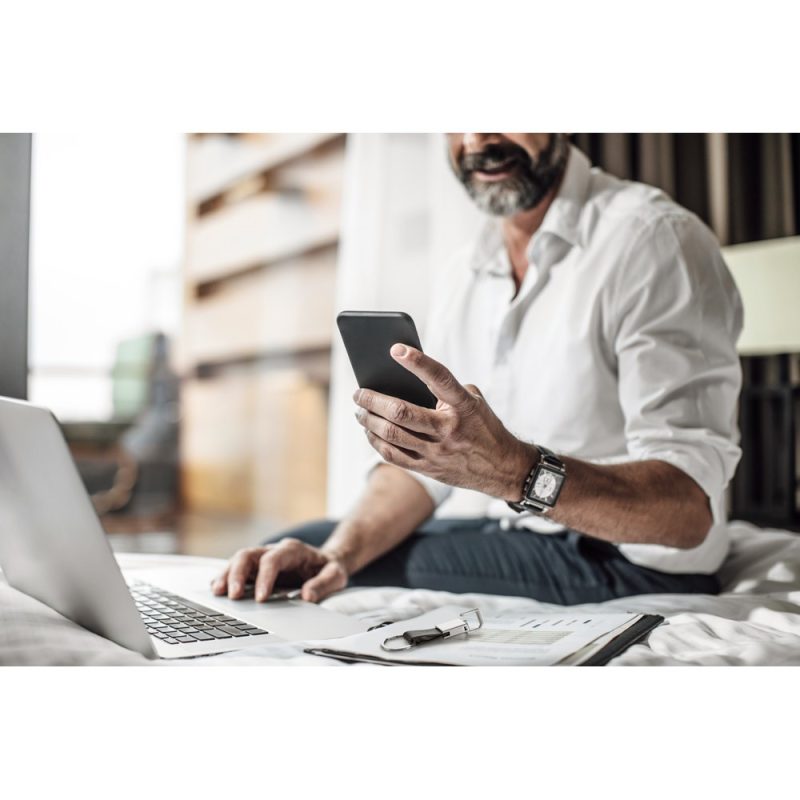 Man using phone and laptop on bed.
