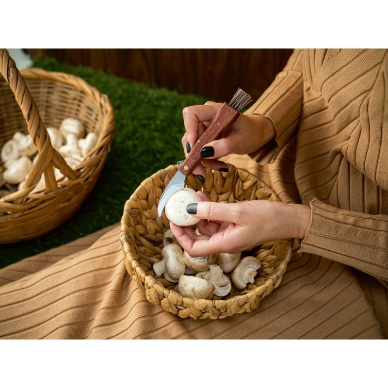 Person cleaning mushrooms in a basket with knife.
