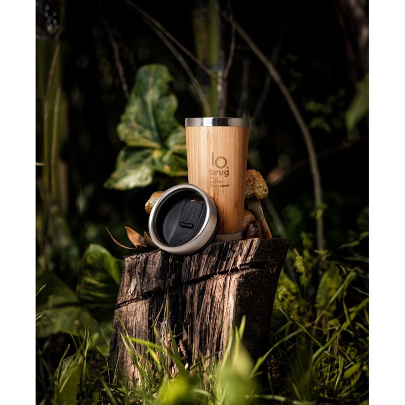 Bamboo coffee cup on wood in forest setting.