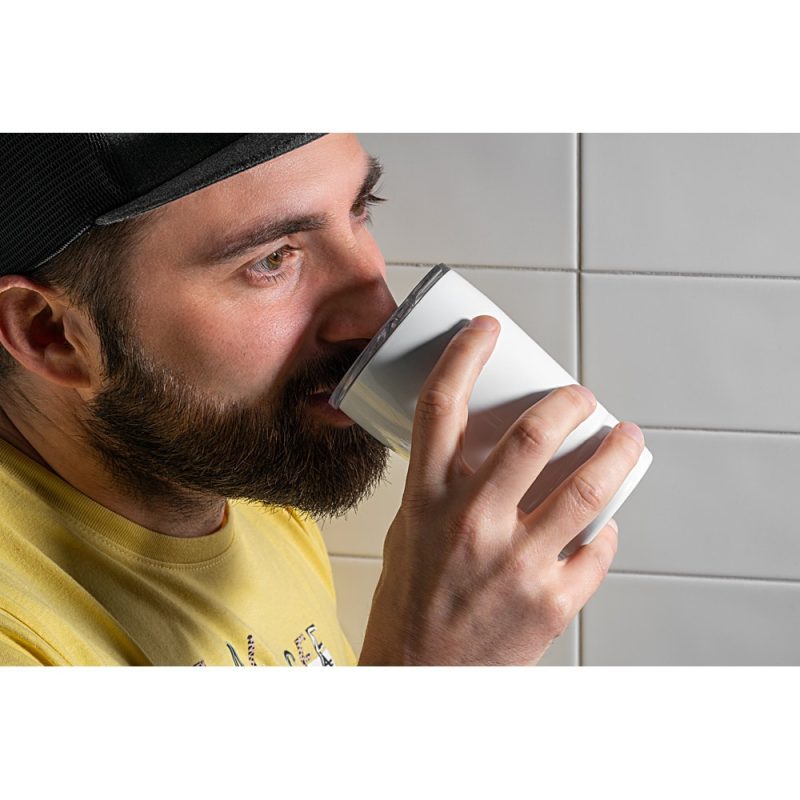 Man drinking from a white cup indoors.