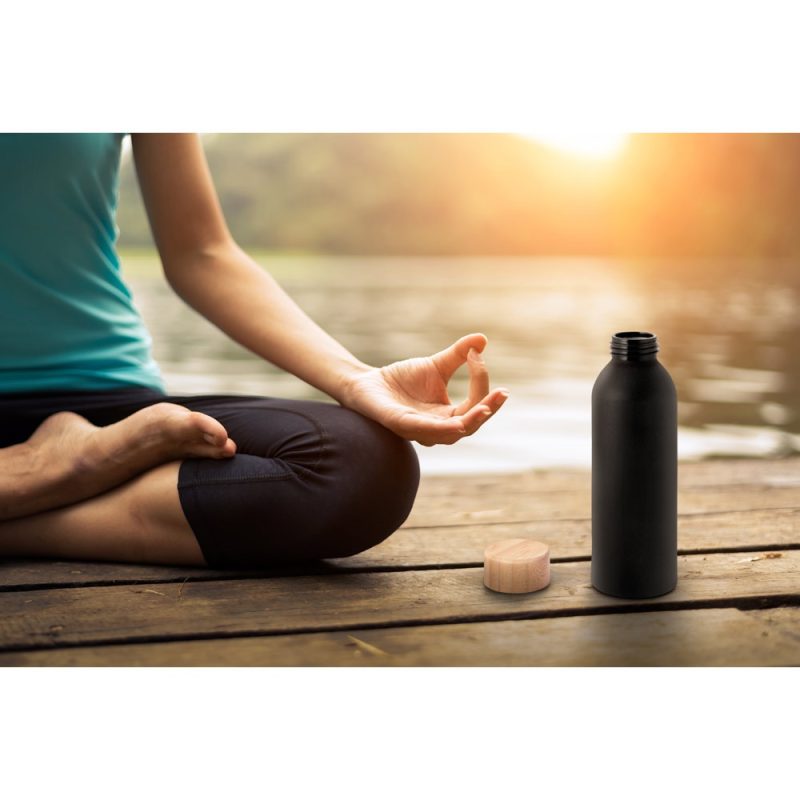 Person meditating by lake with water bottle.