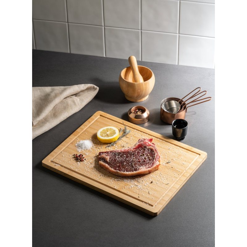Seasoned steak on board with kitchen utensils.