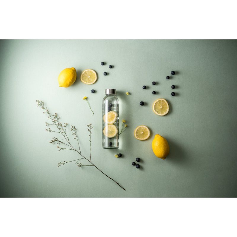 Bottle with lemons, blueberries on green background.