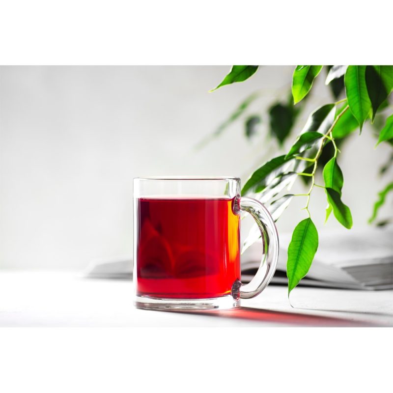 Glass mug of red tea next to green plant.
