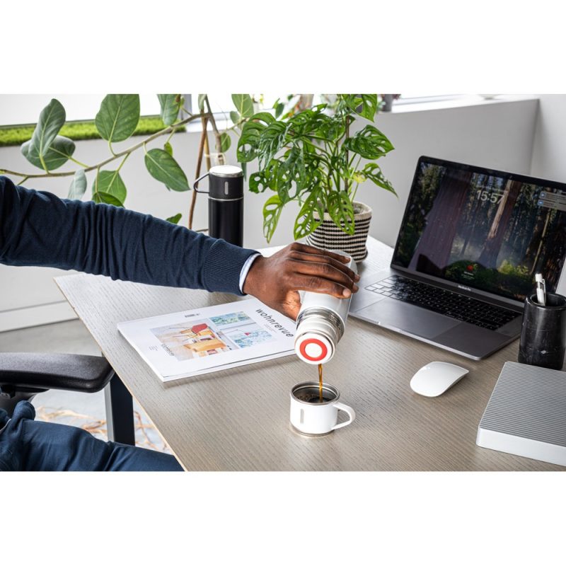 Person pouring coffee at modern workspace with laptop.