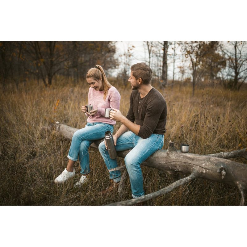 Couple drinking coffee outdoors on fallen tree.