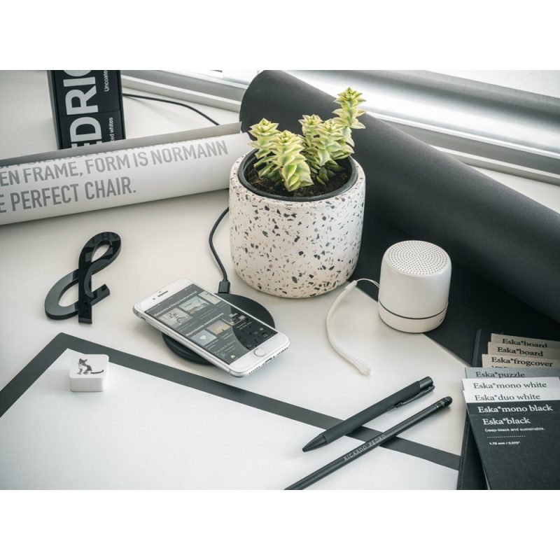 Modern desk with plant, smartphone, speaker and stationery.