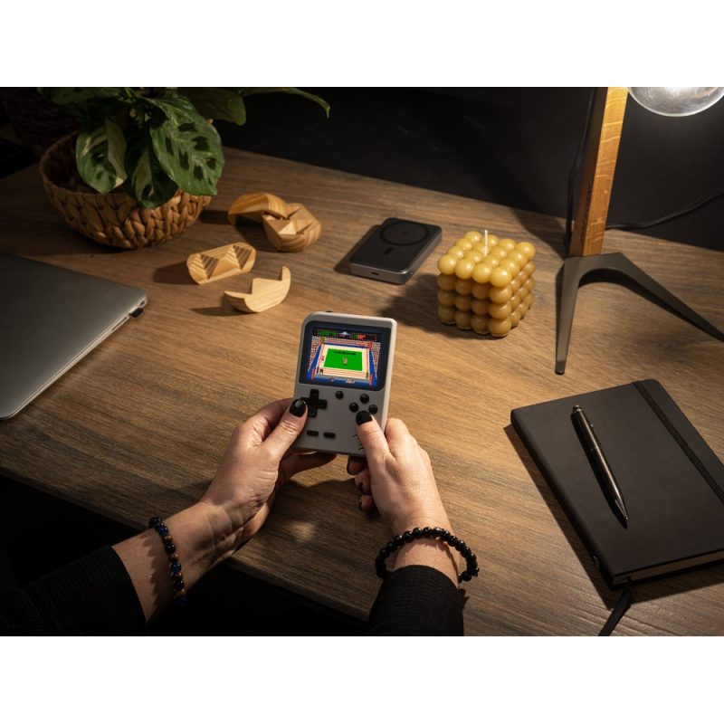 Person playing handheld console on desk.