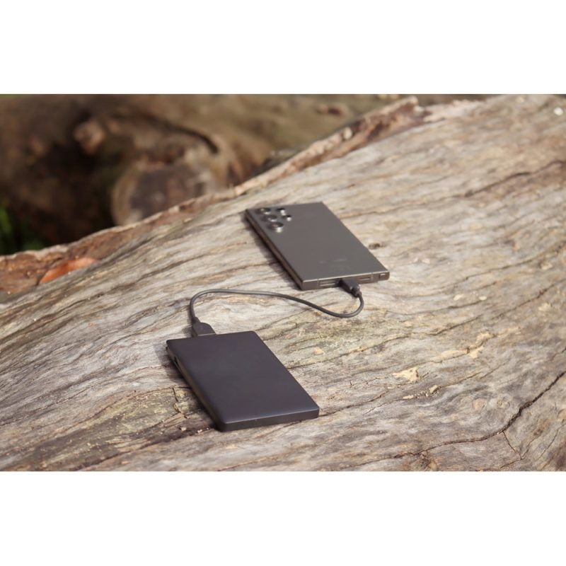 Power bank charging smartphone on wooden surface.