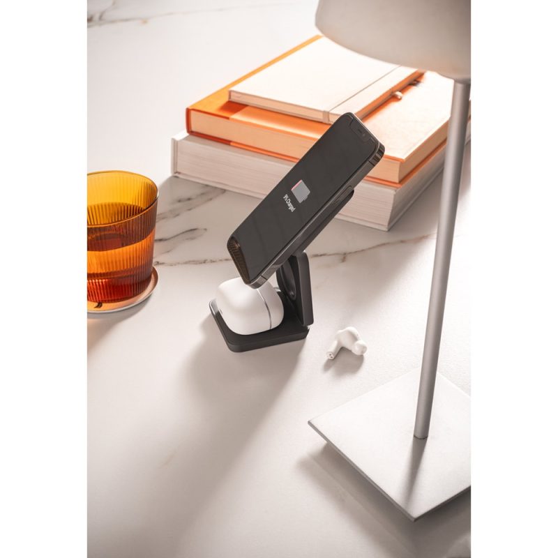 Smartphone on charging stand next to lamp and books.