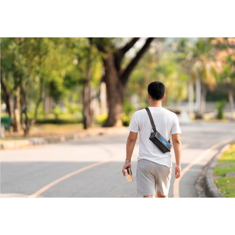 Person walking in sunny park with shoulder bag.