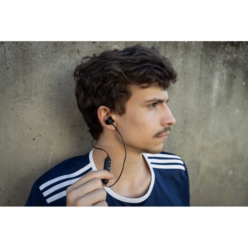 Man wearing earphones against a concrete wall.